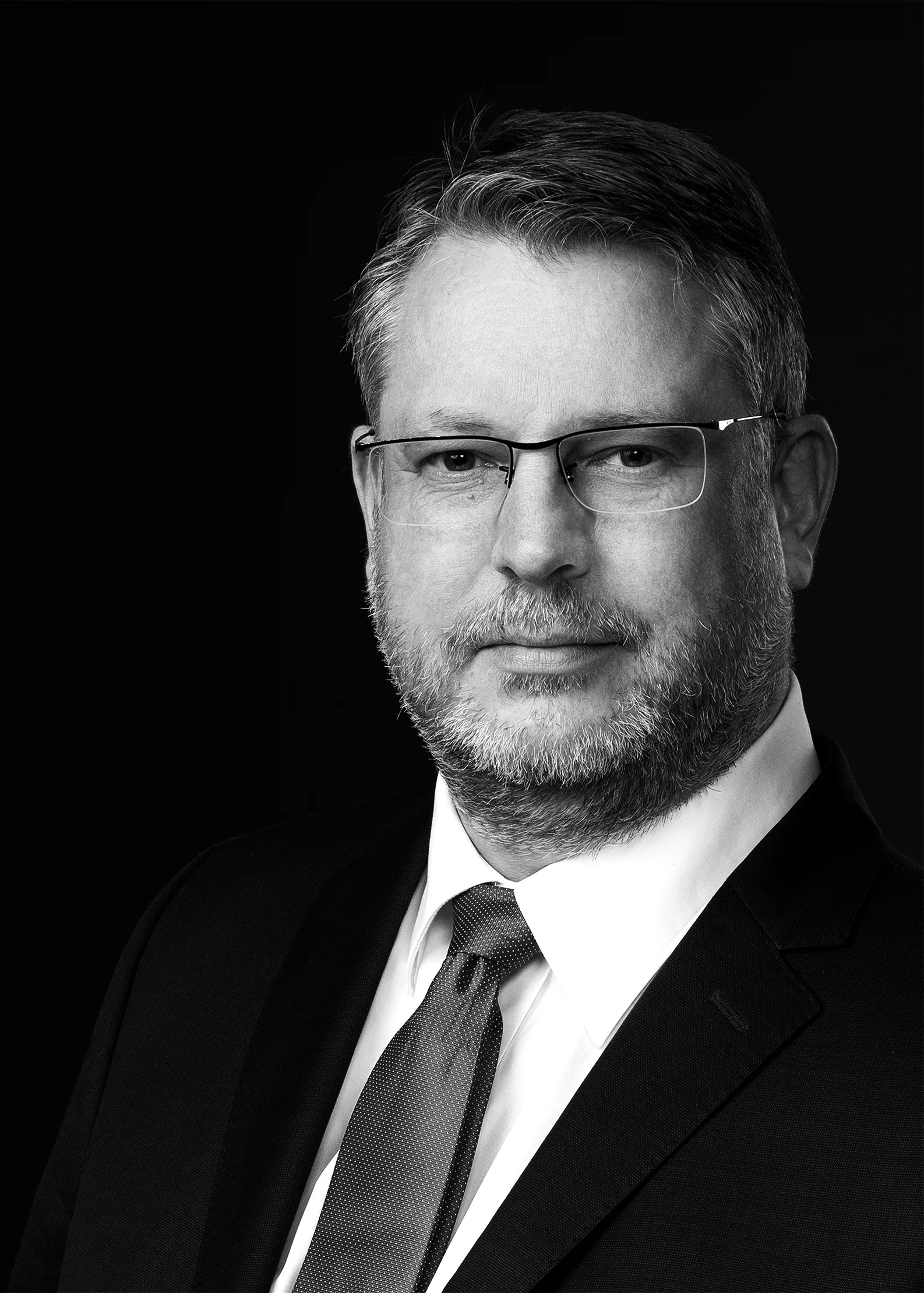 Black and white portrait of a man with glasses in a suit and tie against a dark background